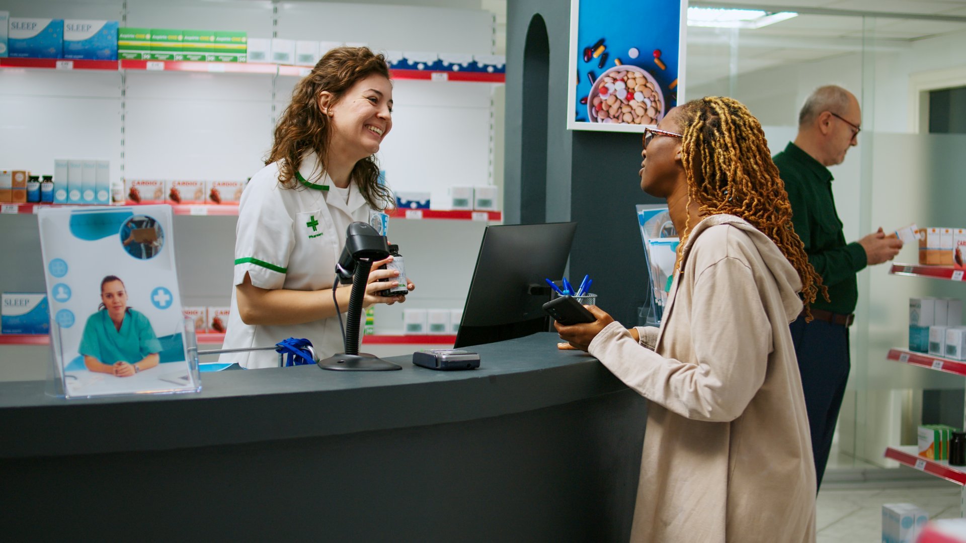 A female pharmacist smiles and answers her customer's questions about their prescription from behind the pharmacy counter.