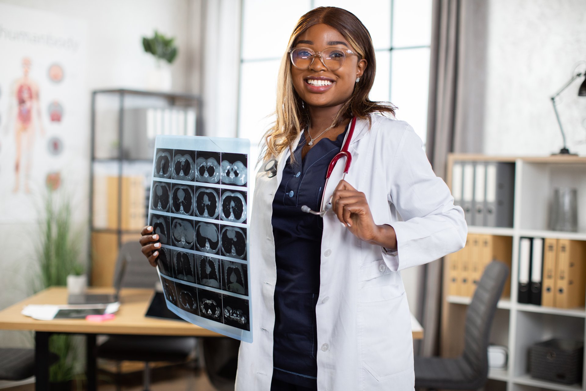 A young female healthcare professional poses while holding a patient's CT scan results.
