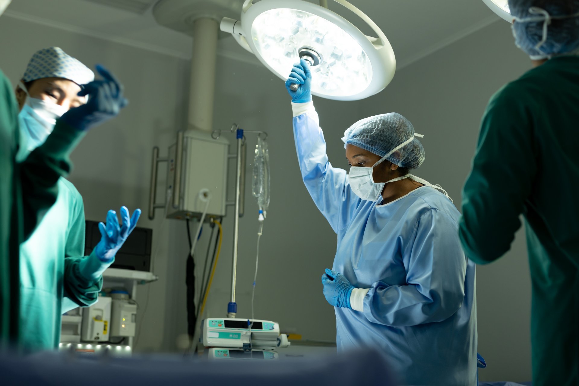 A surgical technologist adjusts an overhead light to help her team prepare for a procedure.