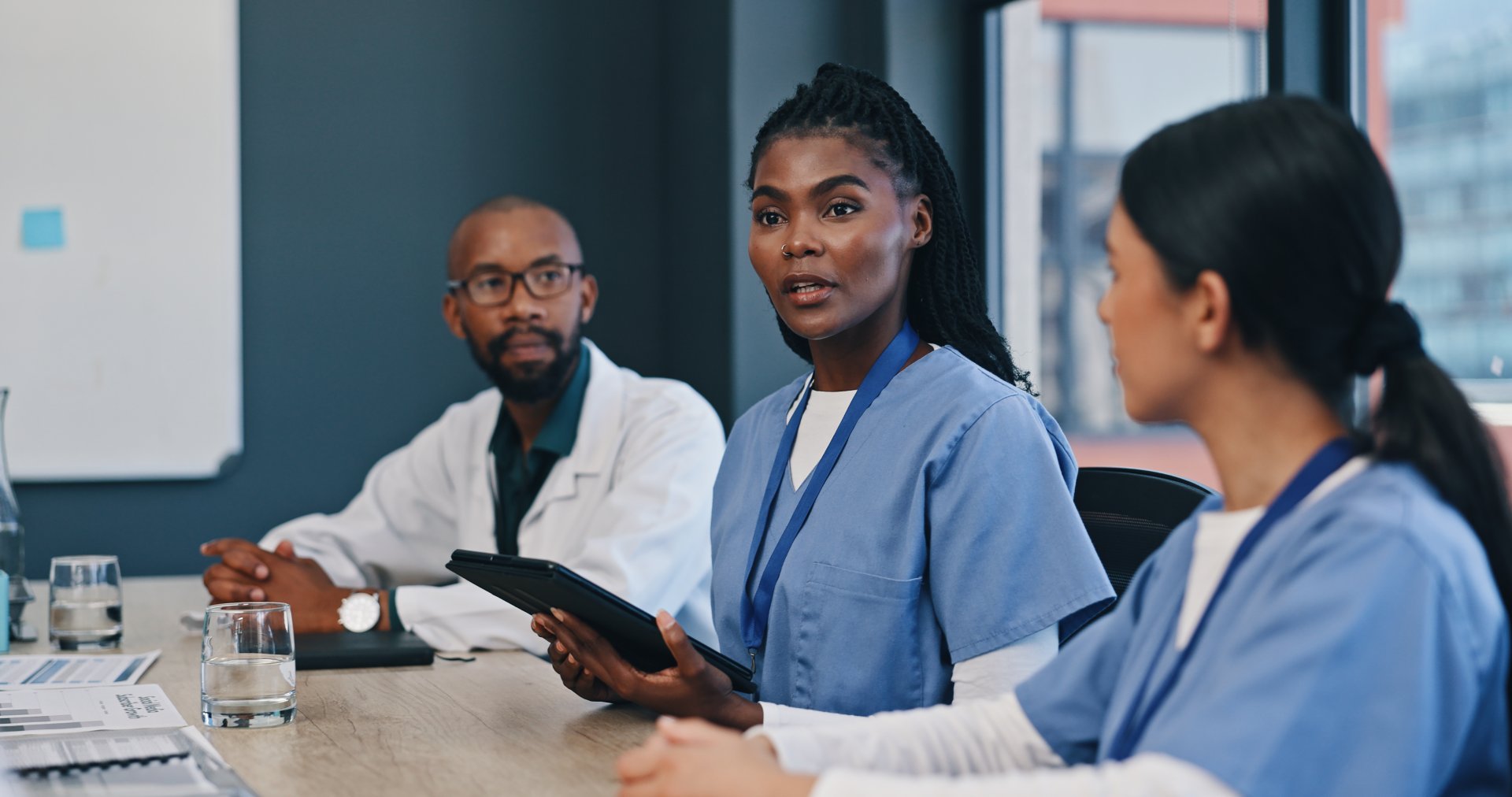 A nurse with a tablet speaks up during a staff meeting