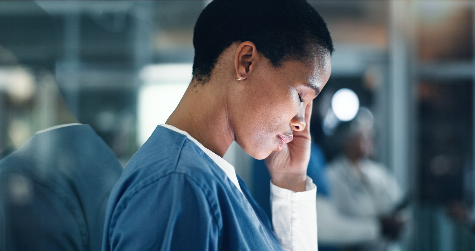 Nurse wearing scrubs holds her hand to her head and closes her eyes