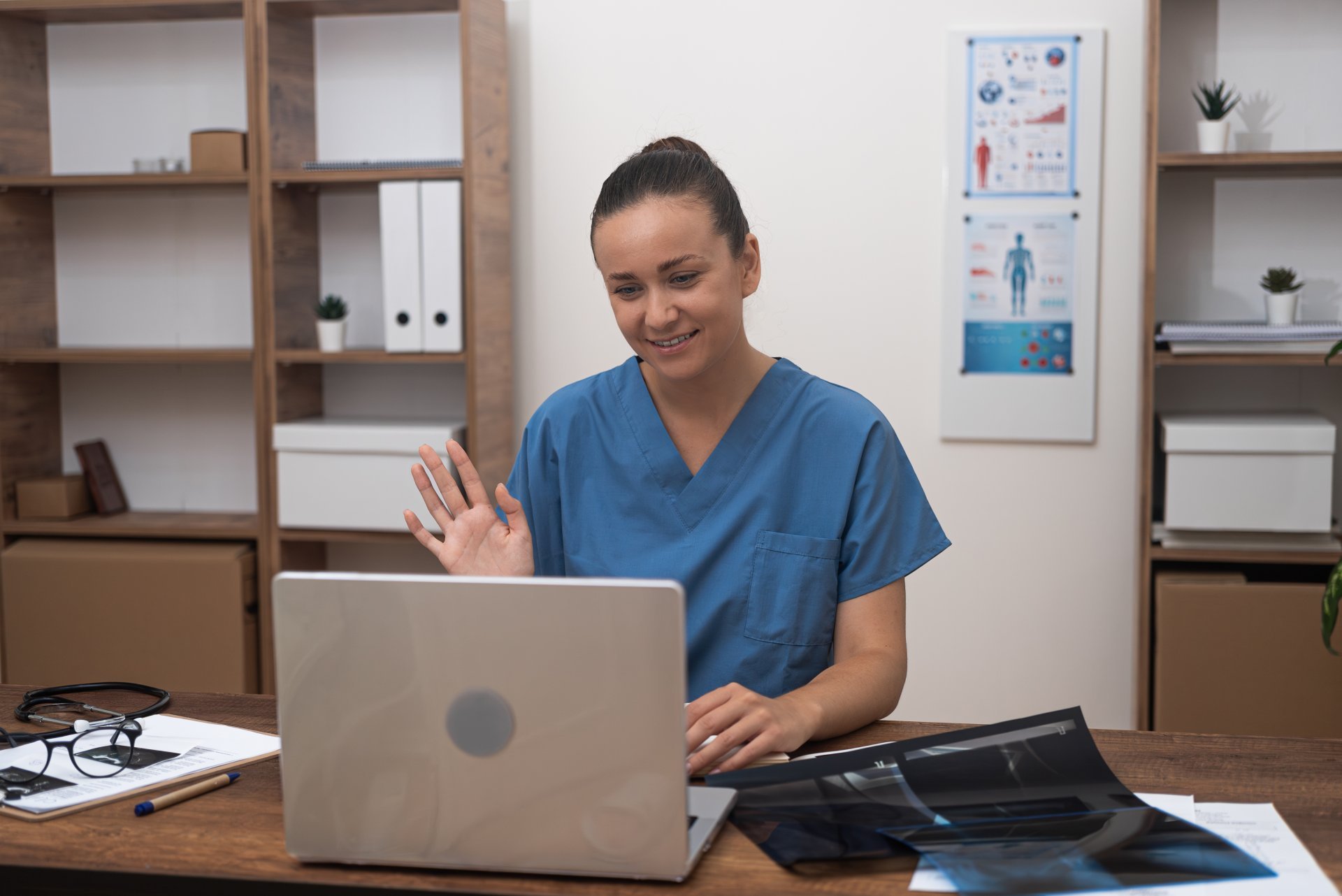 A young female clinician waves to her patient during a remote telehealth appointment.