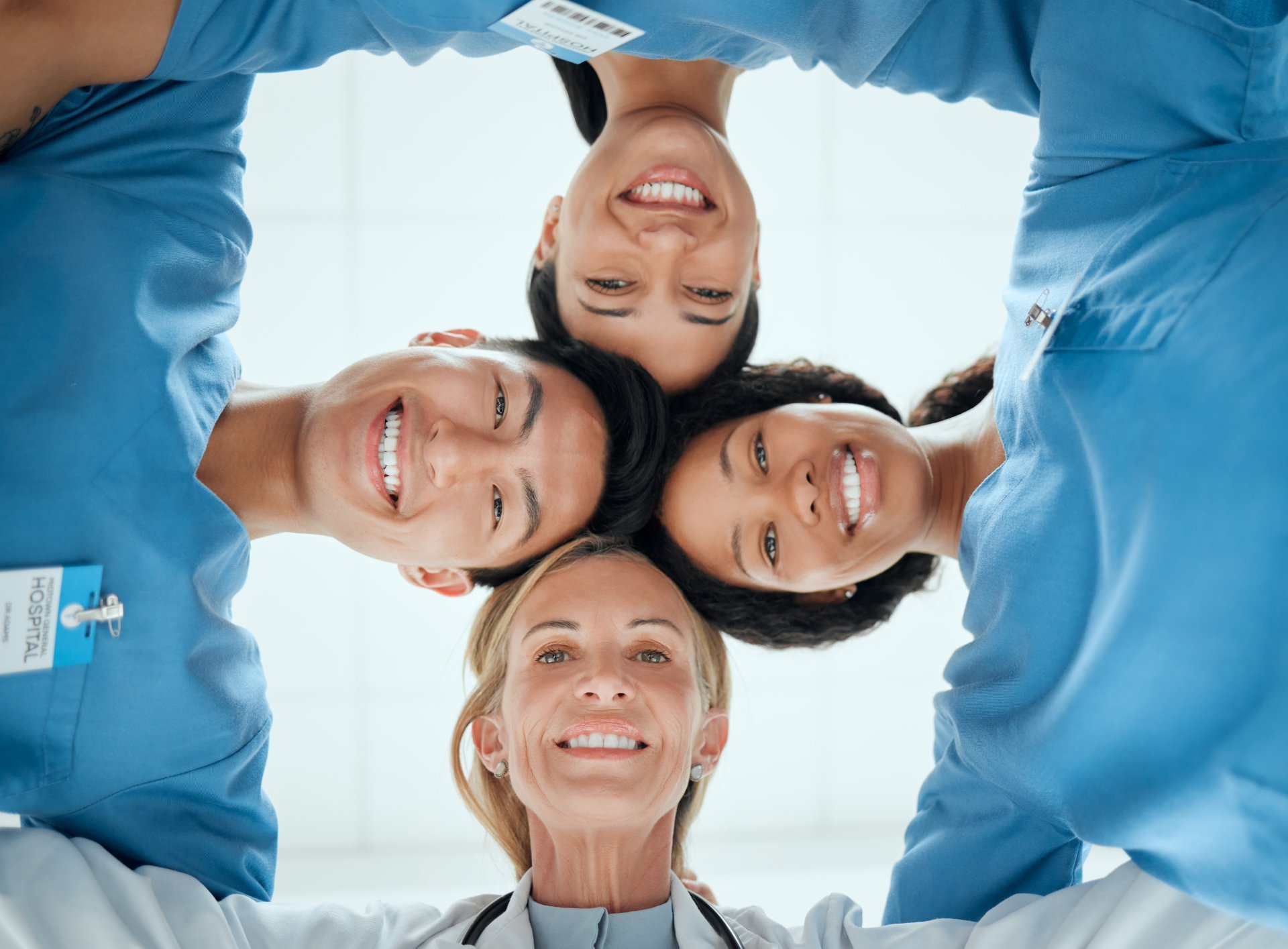 Four smiling healthcare workers huddle with their heads together.