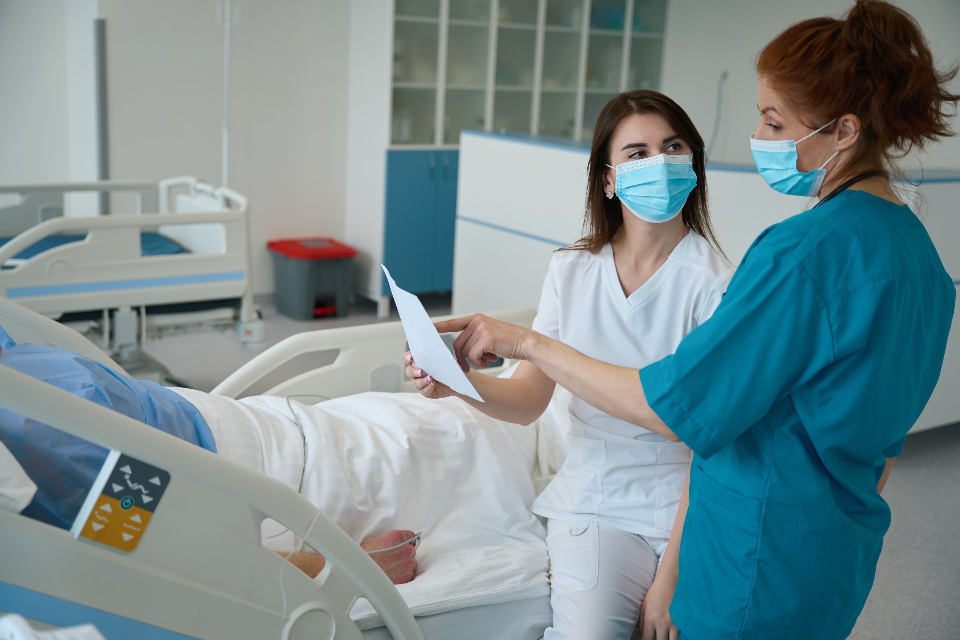 Two female nurses in scrubs and masks discuss protocols with their flu patient Two female nurses in scrubs and masks discuss protocols with their flu patient
