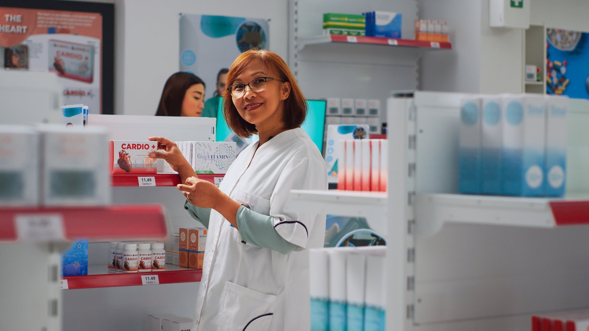 A female pharmacy worker arranges medical products on a shelf in her workplace.