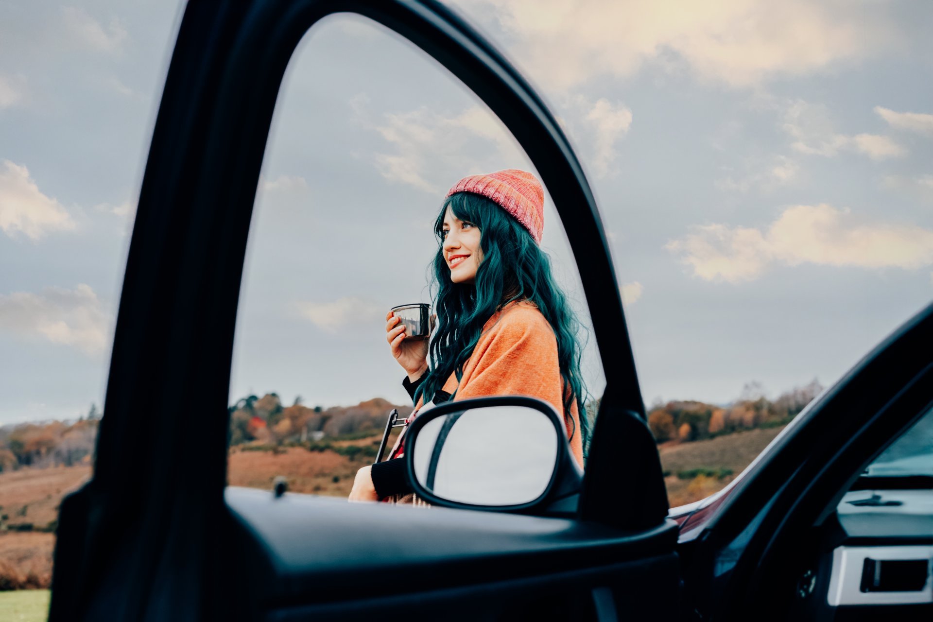 Woman enjoying a warm drink next to her car