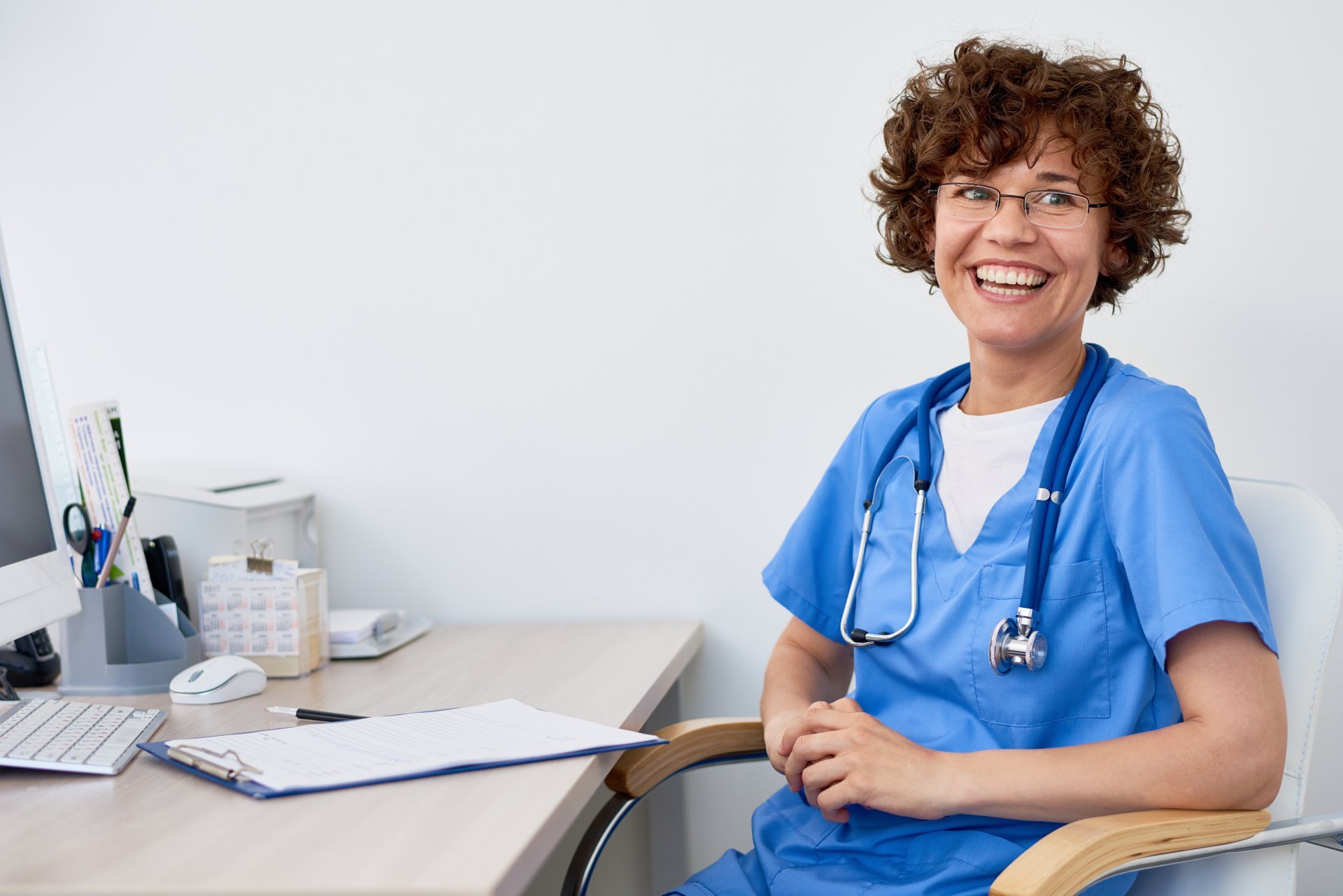 A smiling female clinician sits back in her desk chair.