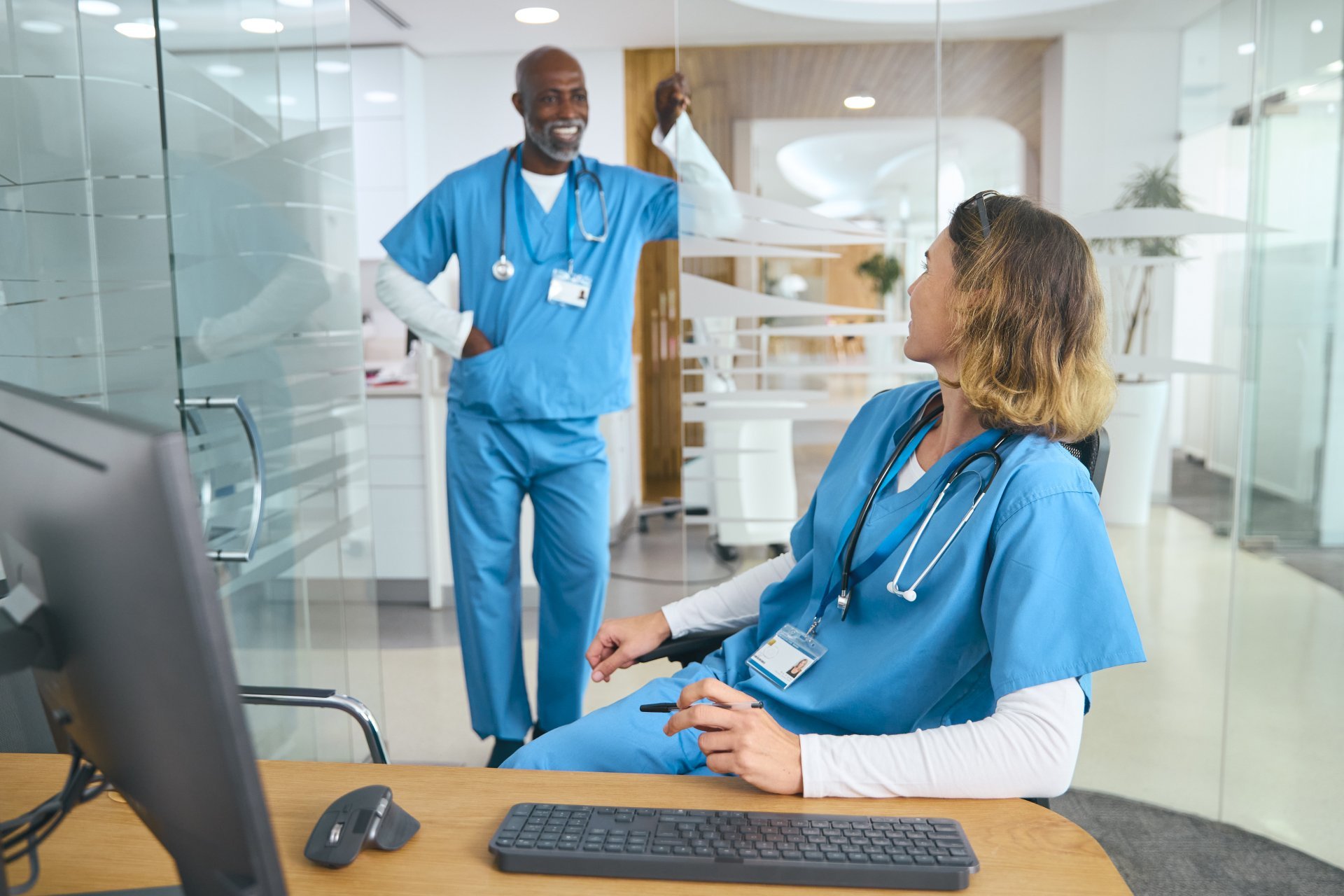 Male and female nurses wearing scrubs and talking in a hospital office