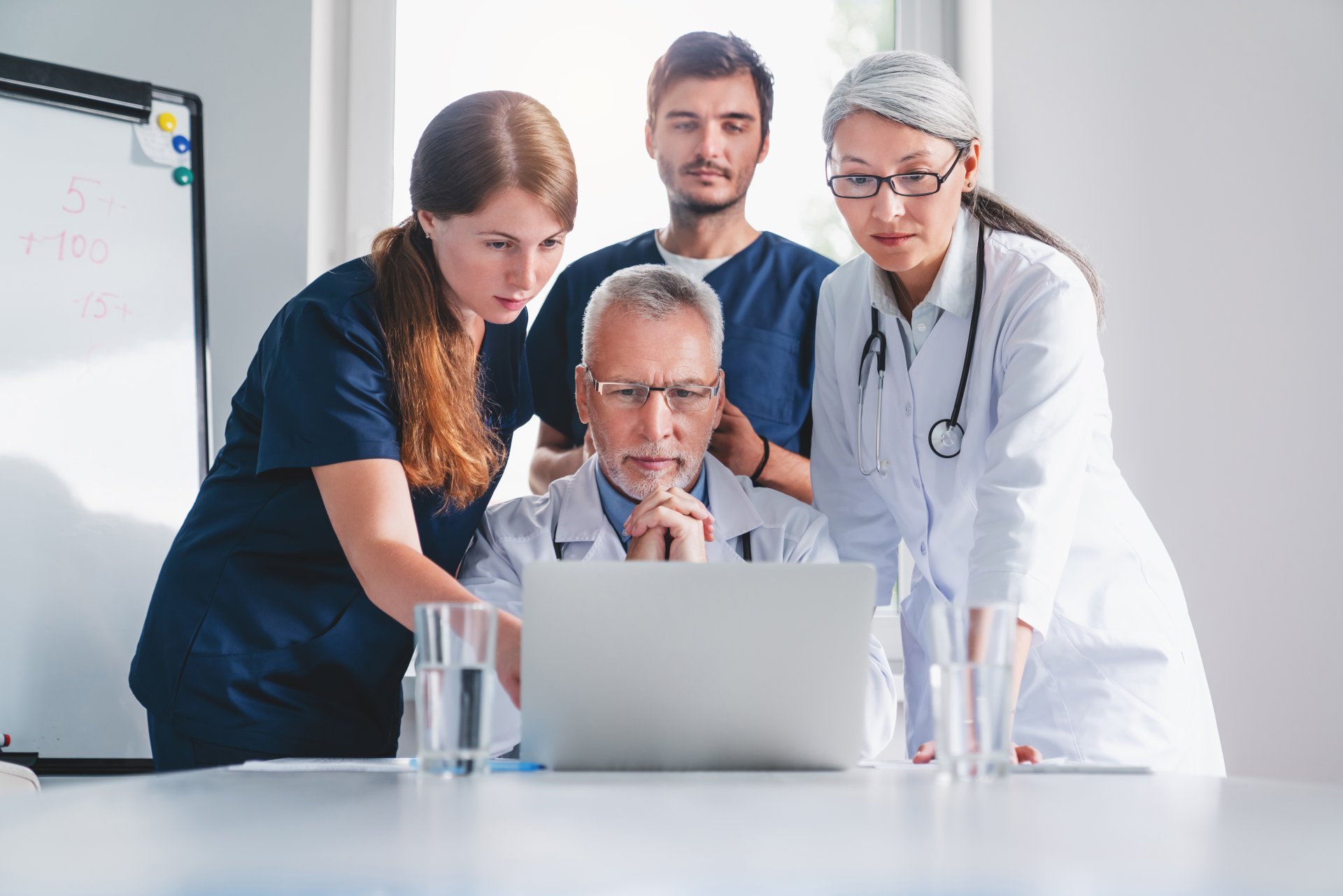A group of doctors and nurses gather around a laptop.