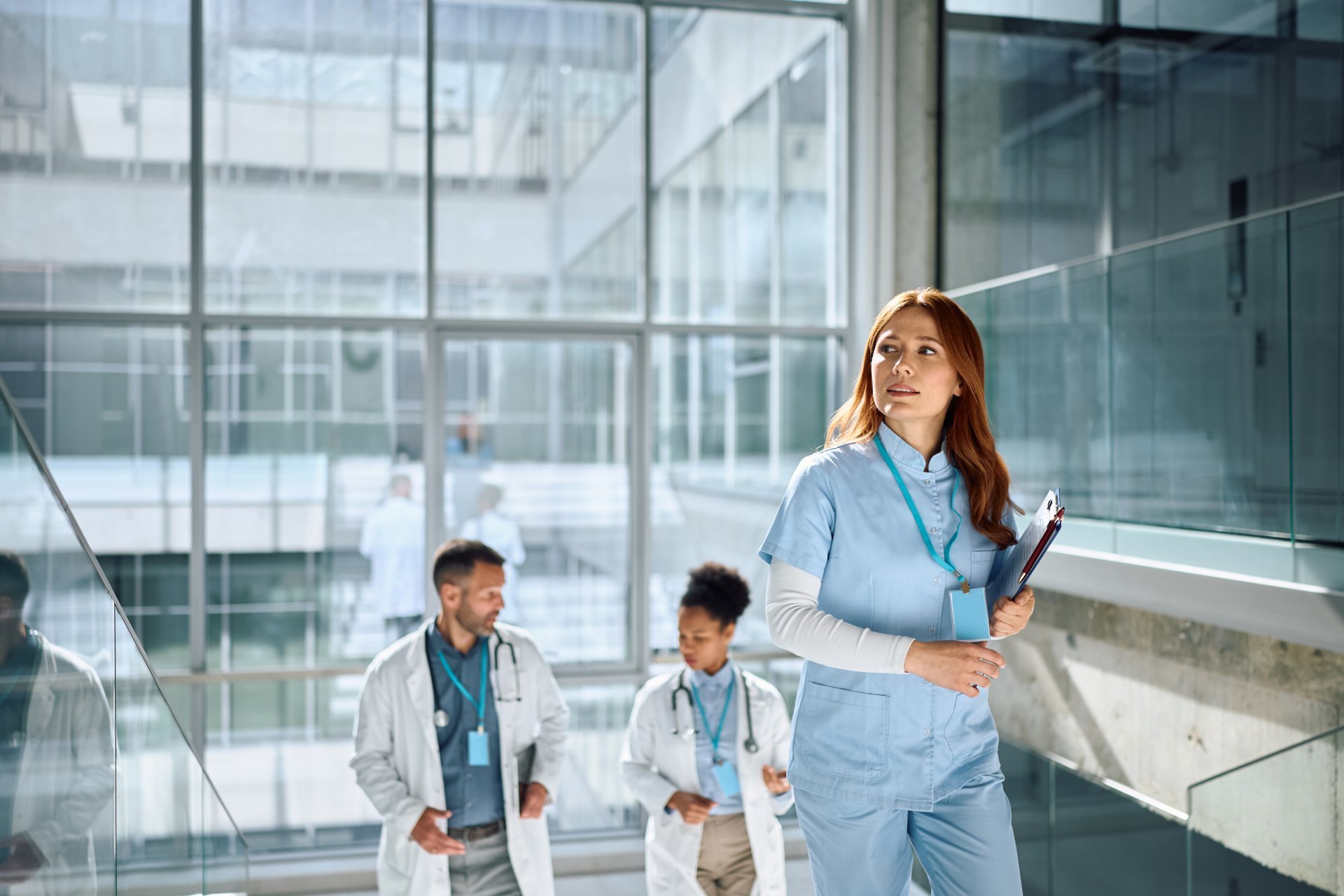Nurse with badge lanyard and papers walking up well lit staircase at hospital