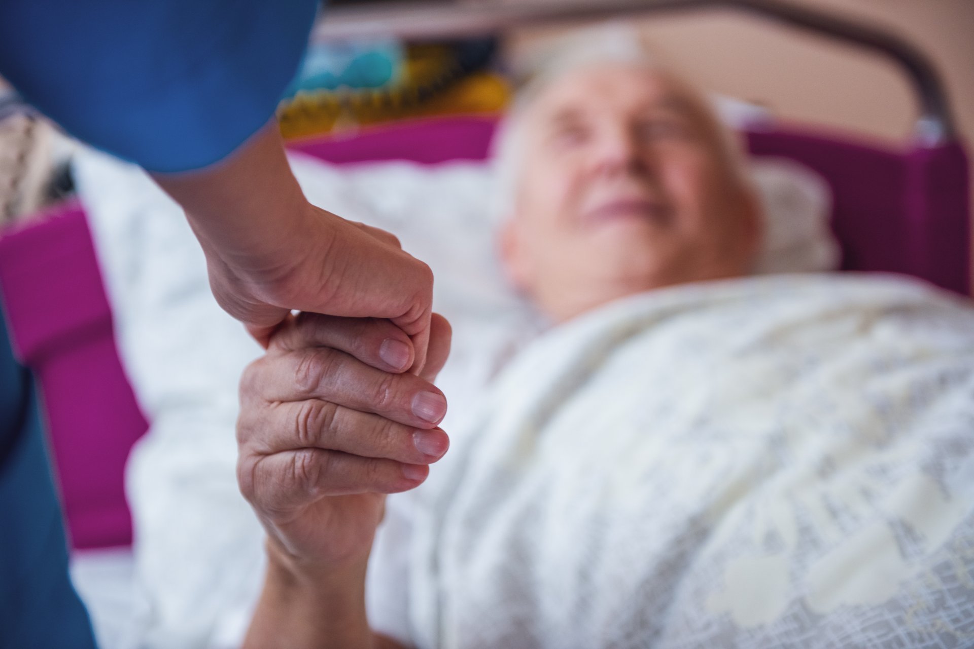 Old man in hospice care holding caregiver's hand