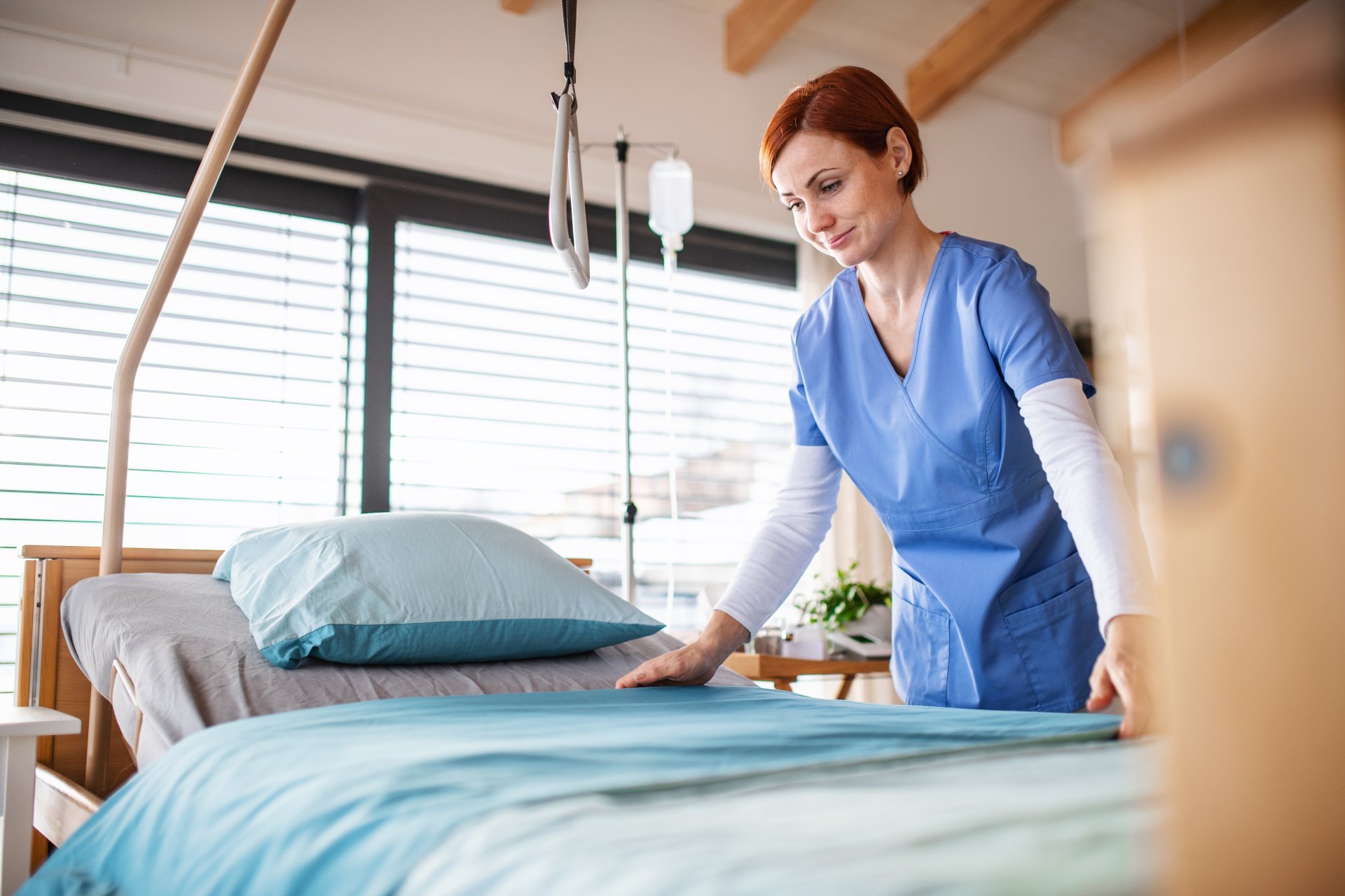 A female nurse changes bedding for a patient.