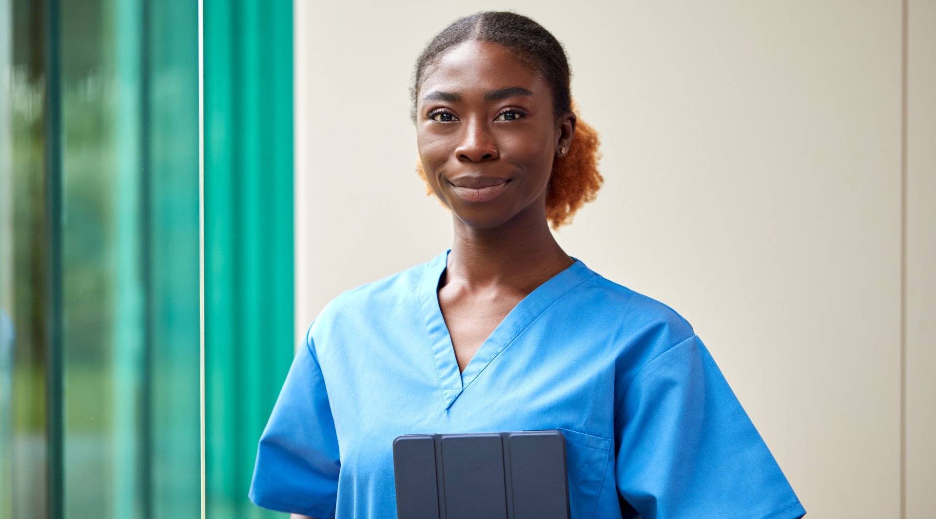 A smiling female clinician wearing scrubs and holding a tablet