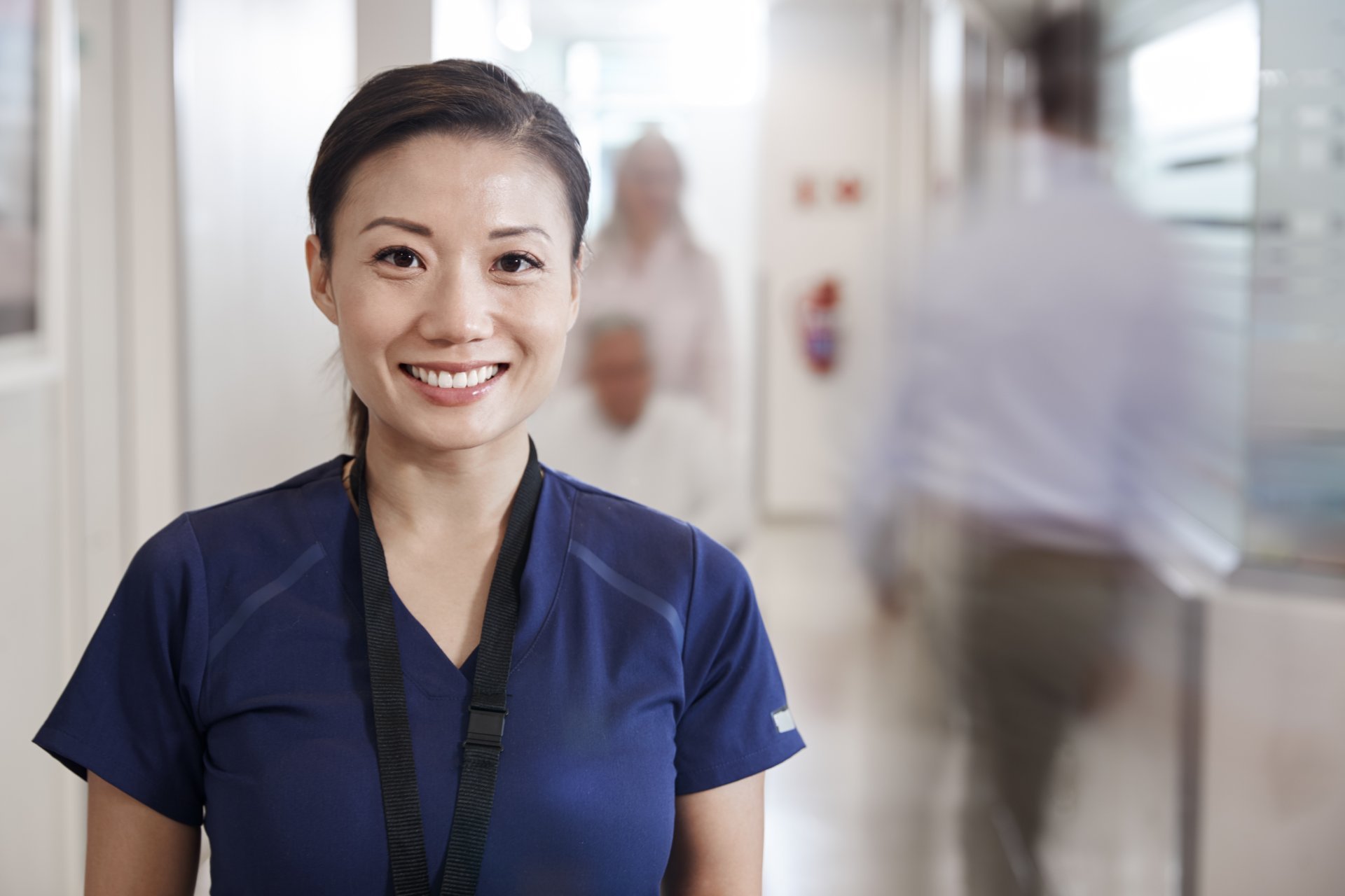 A smiling female nurse stands among a crowded hospital corridor.