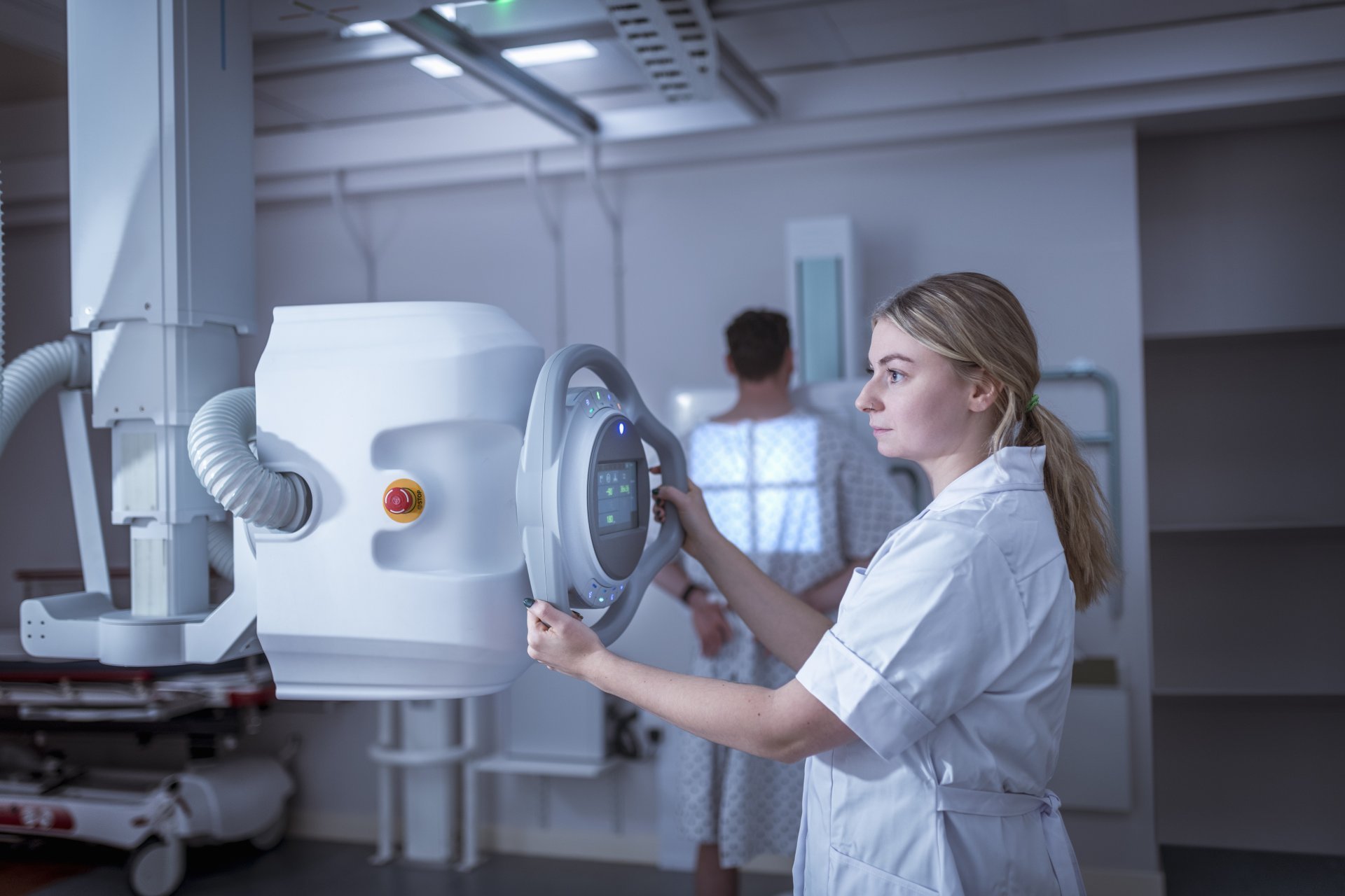 A young female radiologist positions an x-ray machine to examine her patient.