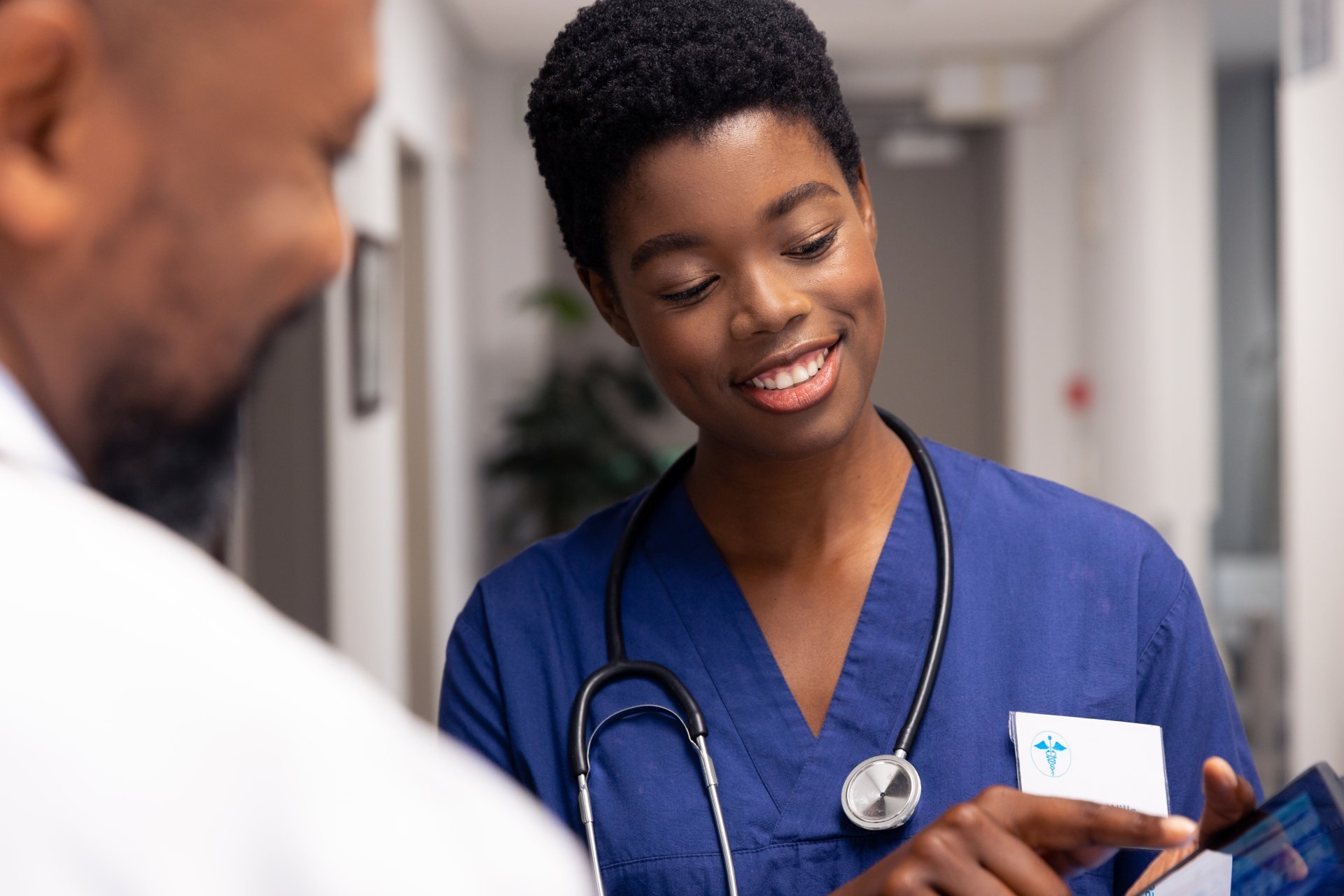 A smiling nurse shows a doctor something on her tablet.