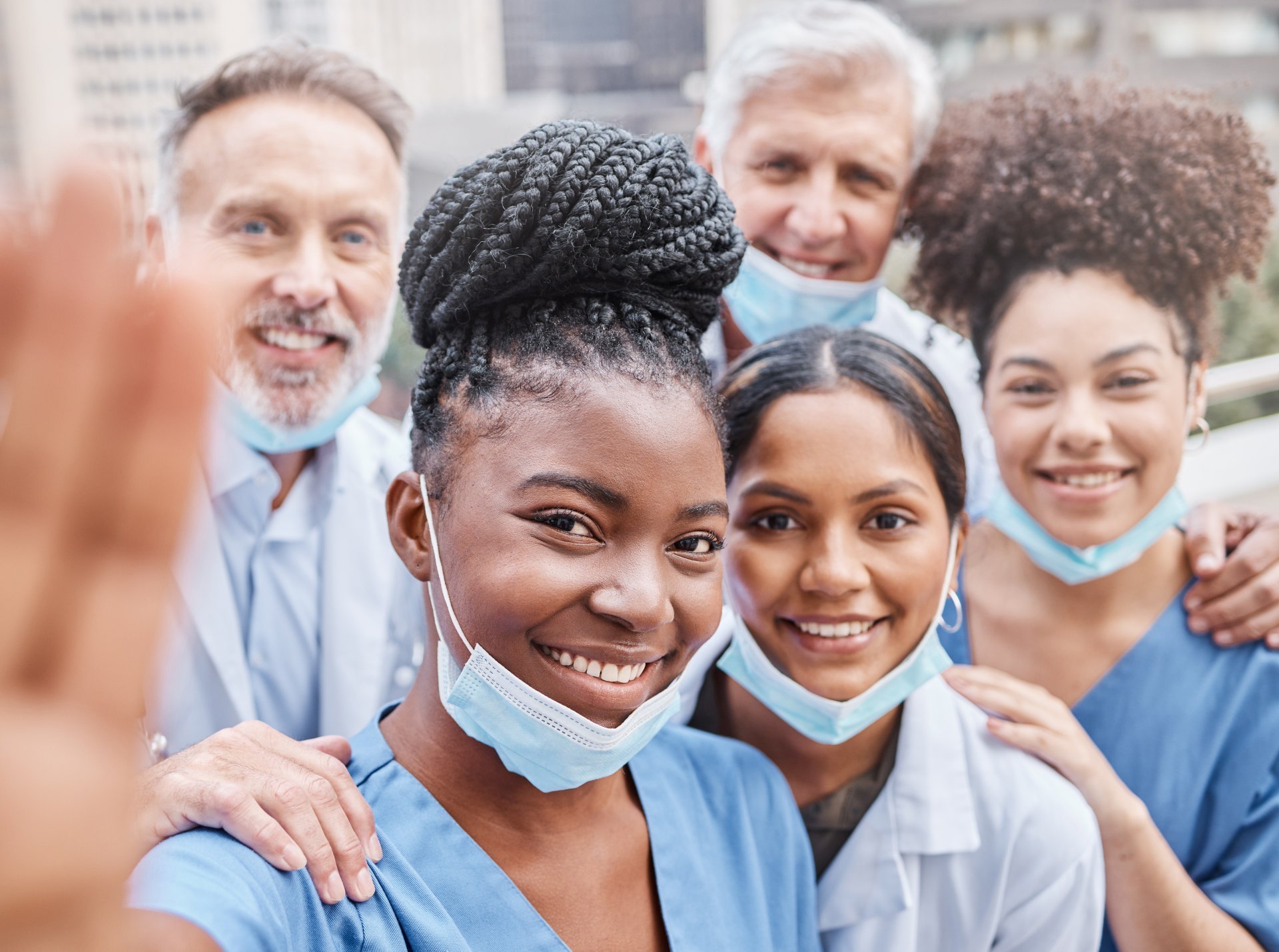 A diverse group of healthcare workers huddles around a camera and smiles.