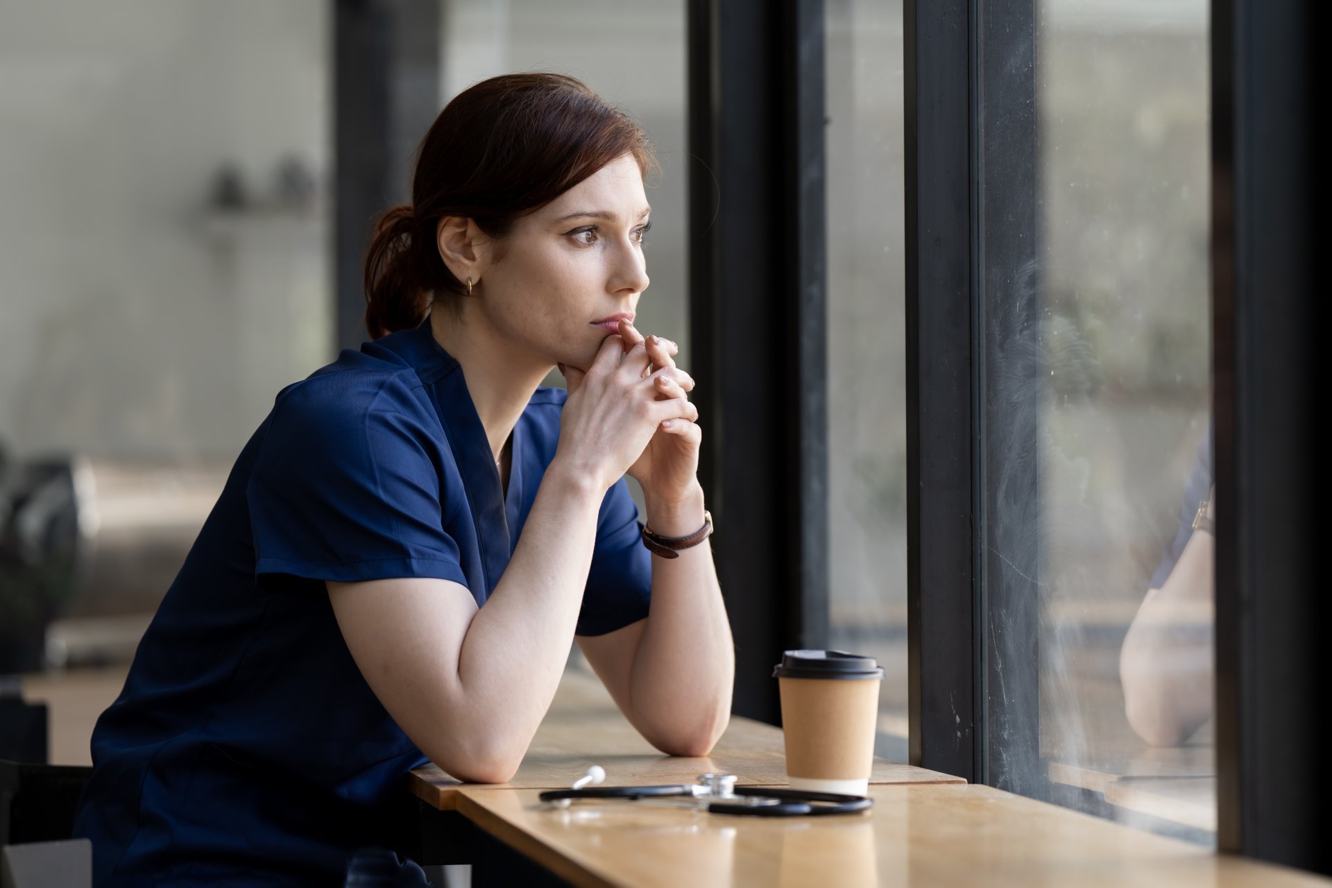 Tired female doctor or nurse with stethoscope looking out a window