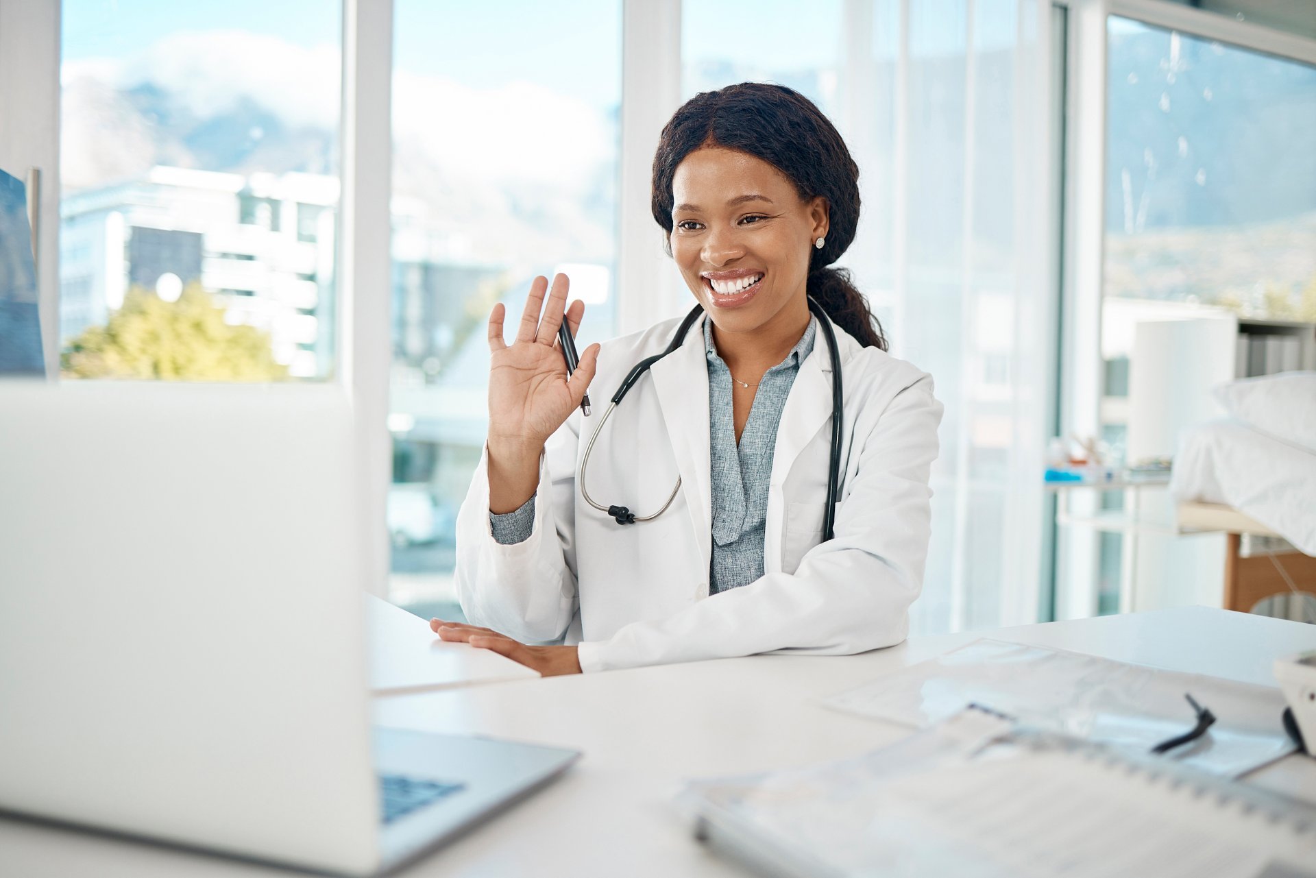 A young female healthcare provider greets her patient during a virtual visit conducted via her laptop.