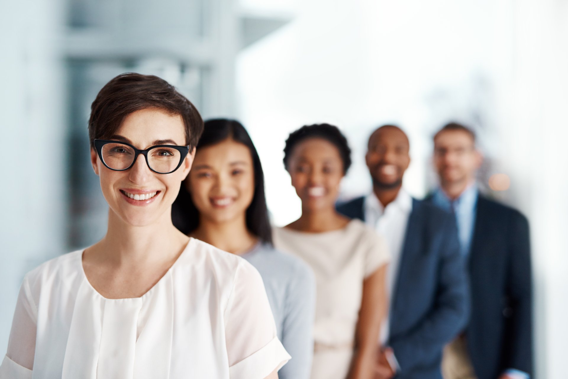 A clear female subject stands in front of four out-of-focus people in business attire.