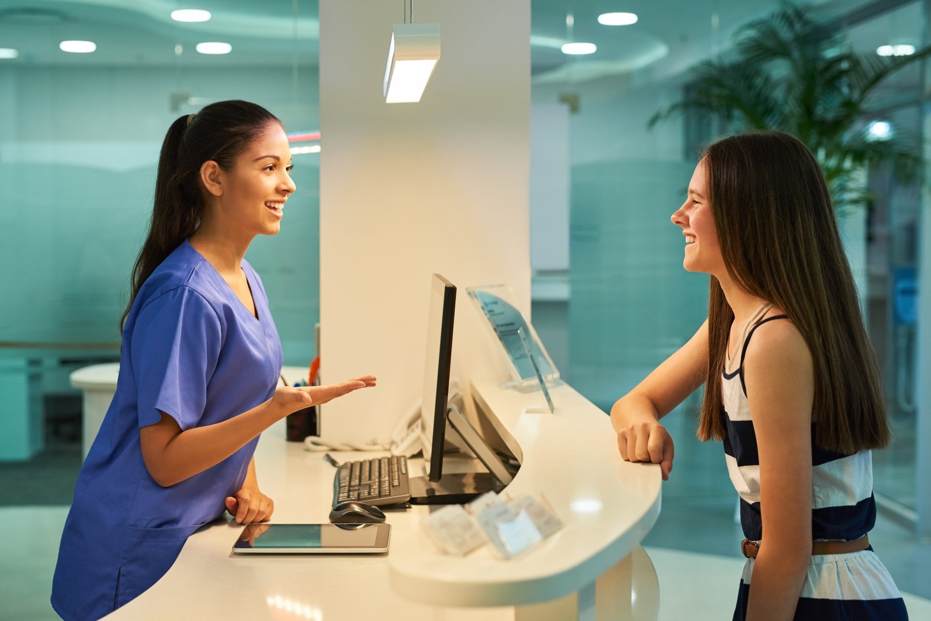 A young female healthcare worker smiles and greets a patient at the front desk of her workplace.