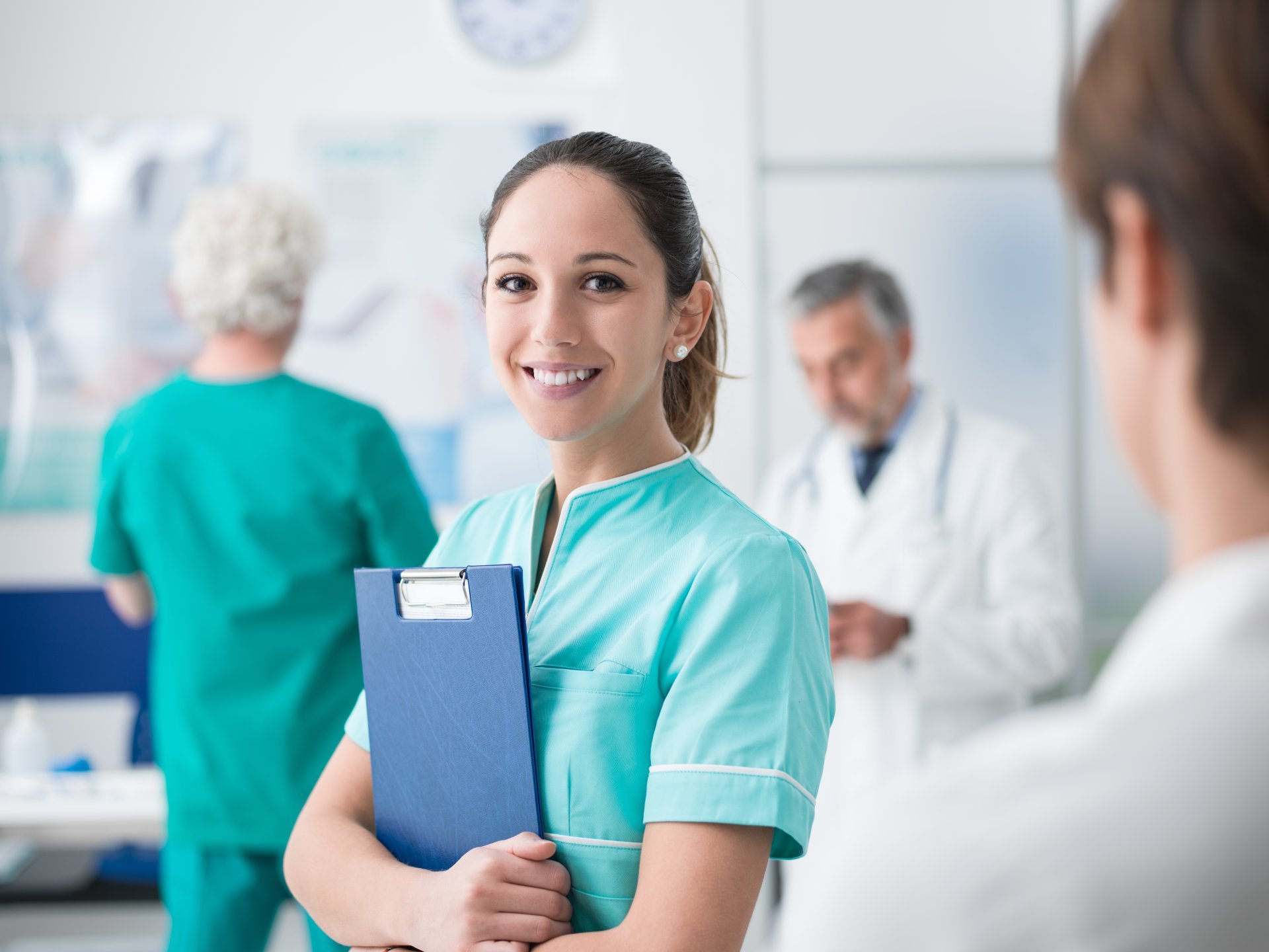 A young female healthcare worker holds a clipboard and smiles.