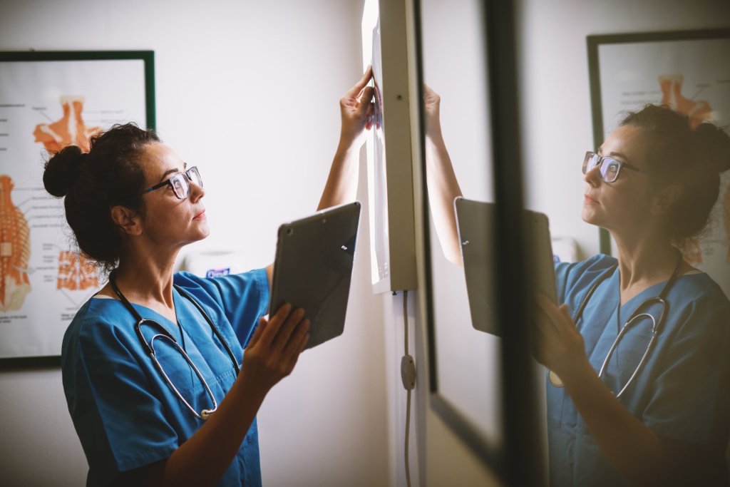 Side view of smiling middle aged nurse checking X-ray in a doctors office.