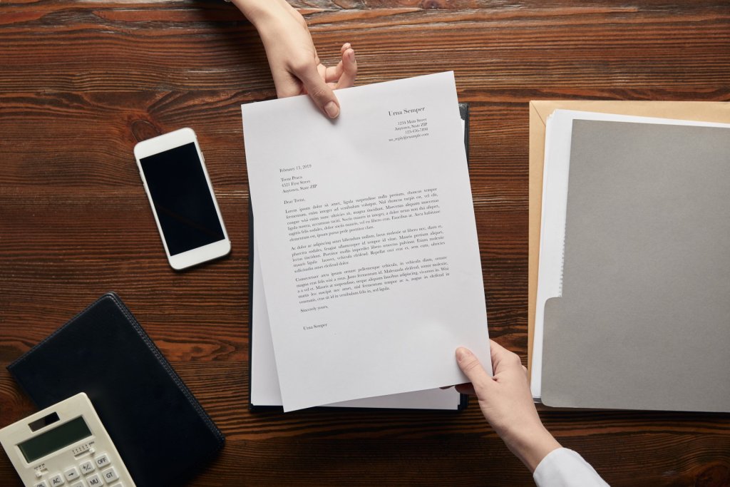 Top view of businesspeople handing paperwork across a desk.